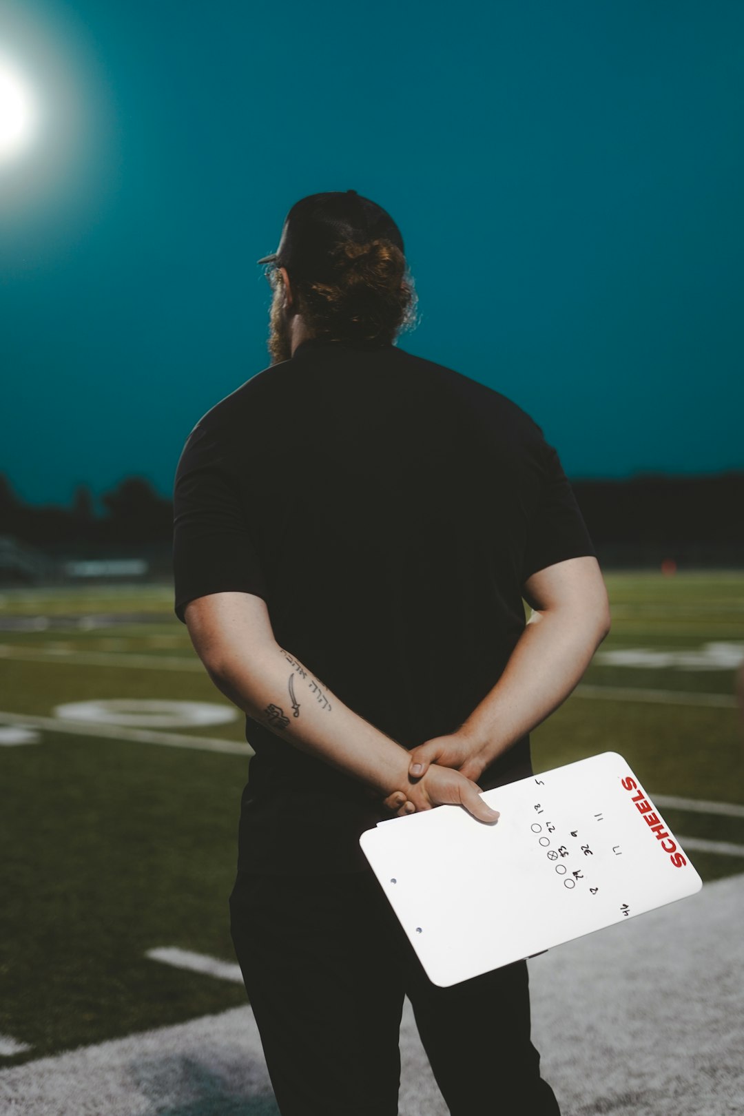 A football coach surveys the field at dusk.